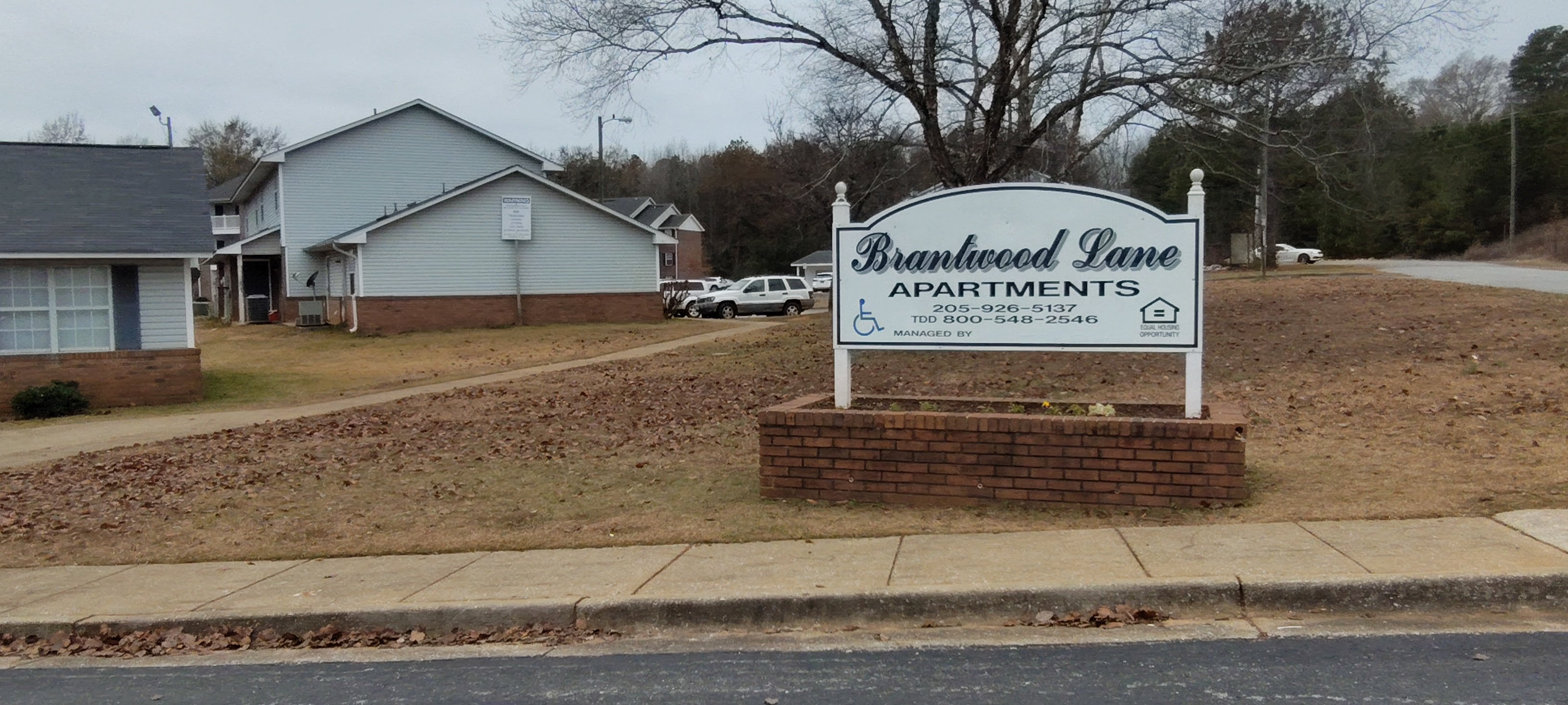 A sign for Brannewood Lane Apartments stands in front of a brick wall.